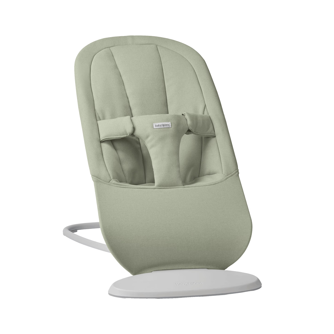 Light green baby bouncer with a padded seat, adjustable straps, and a white curved base.