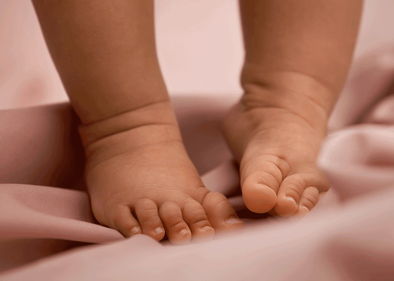 Close-up of baby feet on soft pink fabric, showcasing tiny toes and smooth skin.