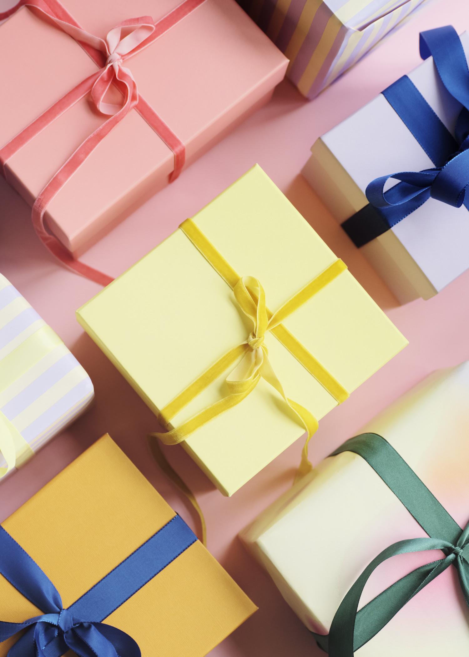 Various gift boxes with colorful ribbons on a pink background, featuring yellow, orange, and pastel-colored wrapping.