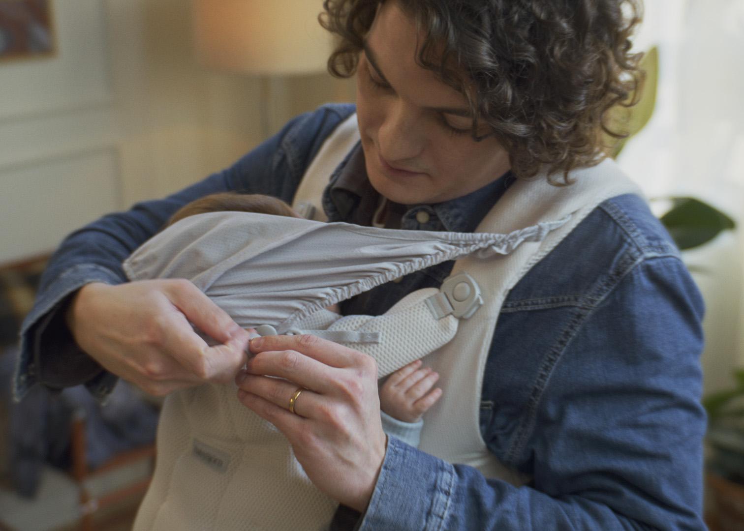 Person adjusting a strap on a baby carrier while the baby sleeps inside.