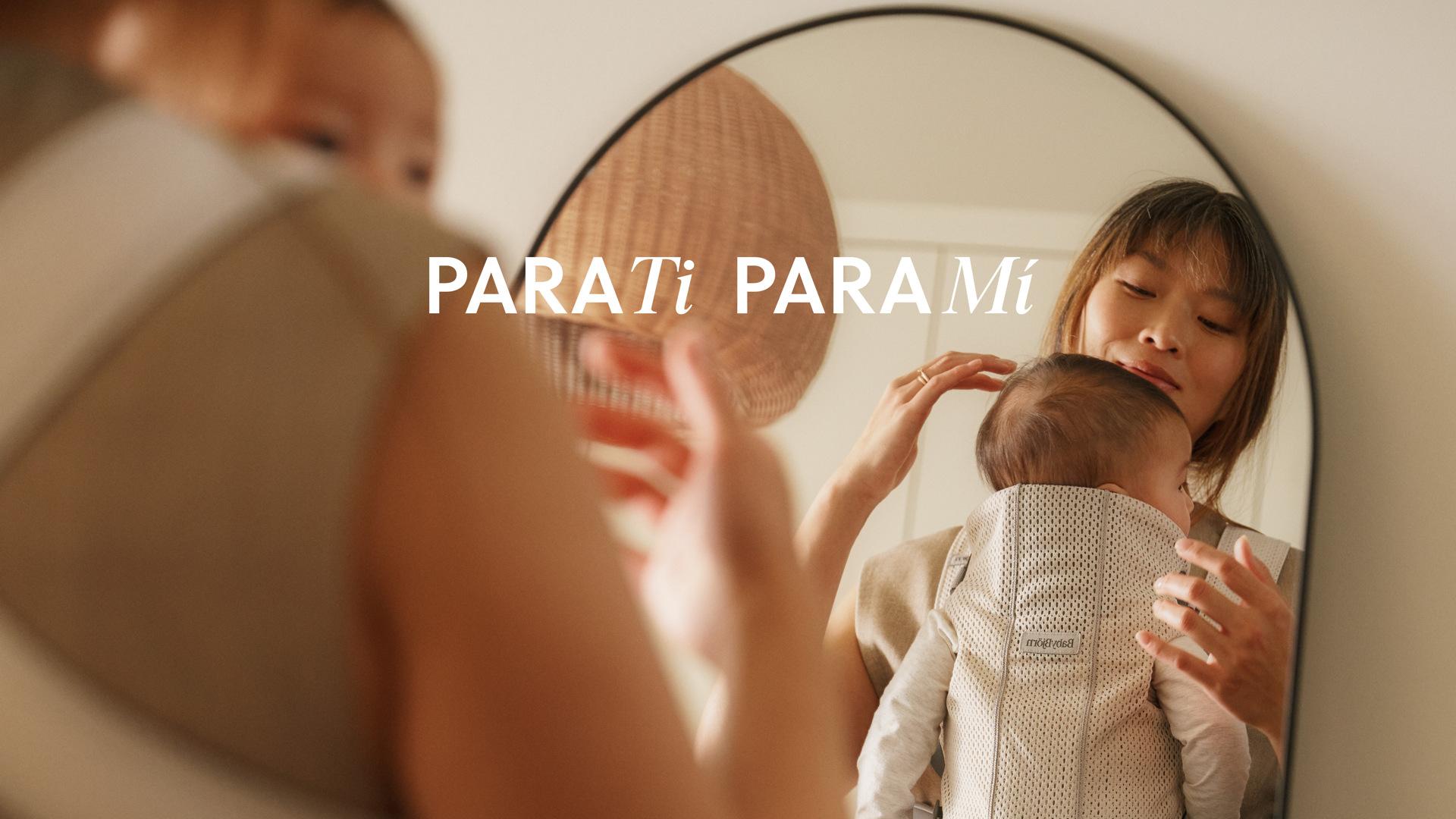A woman holding a baby in a carrier, standing near a mirror, with the text "PARA Ti PARA Mí" over the reflection.